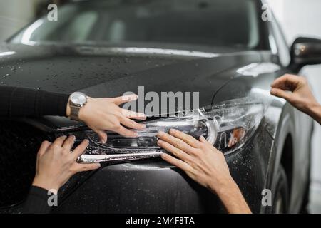 Nahaufnahme des PPF-Einbauverfahrens an einem Frontscheinwerfer. PPF ist eine Lackschutzfolie, die den Lack vor Kratzern und Steinschlag schützt. Konzept von: Wächter, Schutz, Auto, neu, Arbeit. Stockfoto