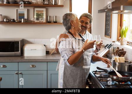 Wein passt am besten zu Romantik. Ein glückliches, reifes Paar, das mit Wein anstoßen und zu Hause zusammen eine Mahlzeit kochen. Stockfoto