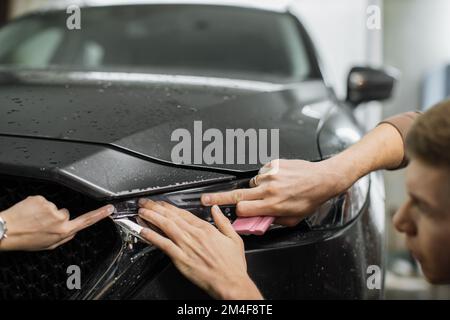 Nahaufnahme der Montage der Schutzfolie am Frontscheinwerfer eines modernen Luxusfahrzeugs. PPF, Polyurethanfolie, die auf die Fahrzeugoberfläche aufgetragen wird, um den Lack vor Steinschlag, Insektenspritzer und Abrieb zu schützen. Stockfoto