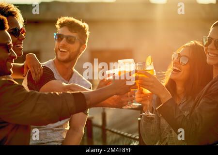 Zusammen ist unser Lieblingsort. Eine Gruppe junger, vielfältiger Freunde, die einen Drink genießen und den Tag draußen auf einem Dach verbringen. Stockfoto