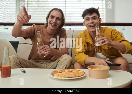 Fröhliche junge Männer, die Bier trinken, wenn sie zu Hause ein Fußballspiel sehen Stockfoto