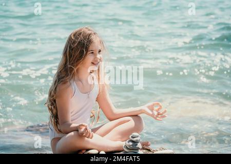 Eine Frau mit Tochter hat eine Biltsteinpyramide am Meer an einem sonnigen Tag auf blauem Meereshintergrund. Frohe Familienferien. Kieselstrand, ruhiges Meer. Konzept Stockfoto