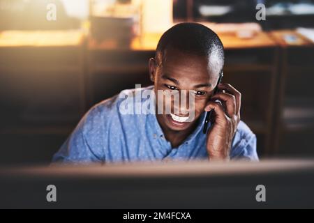 Es läuft gut. Ein gutaussehender junger Geschäftsmann, der nachts in einem modernen Büro ein Mobiltelefon benutzt. Stockfoto