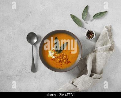 Kürbiscremesuppe mit Salbei und Chikerbsen und Feta auf einem Teller auf einem kokten Hintergrund, Draufsicht Stockfoto