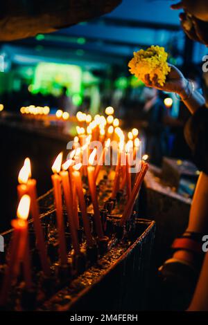 Ein flacher Brennpunkt der Beleuchtung von Votivkerzen mit Besuchern im Hintergrund in einer Kirche Stockfoto