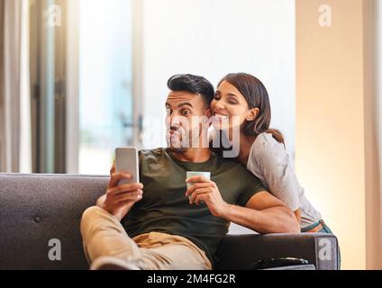 Glück ist, zusammen dumm zu sein und es total zu genießen. Ein junges Paar, das zu Hause Selfies macht. Stockfoto