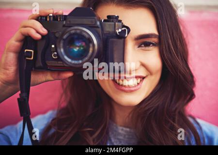 Kameras sind praktisch, um Erinnerungen festzuhalten. Porträt einer schönen jungen Frau, die eine dslr-Kamera hält und draußen gegen eine Wand posiert. Stockfoto