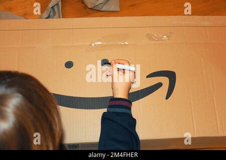 Dezember 19. 2022, Florenz, Italien, gemischter kleiner Kleinkinder, der nach Erhalt der Sendung Augen in einem Karton mit „Amazon“ malt. Stockfoto