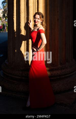Junge Frau im langen roten Kleid im Palace of Fine Arts in San Francisco | Goldene Stunde Stockfoto