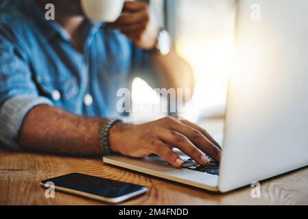 Zusätzliche Arbeit außerhalb des Büros erledigen. Nahaufnahme eines unbekannten Mannes, der Kaffee trinkt, während er in einem Café arbeitet. Stockfoto