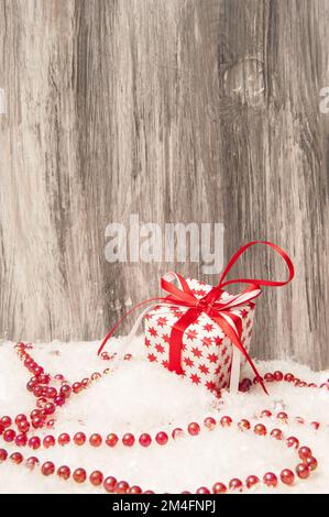 Silvestergeschenk mit roter Schleife und Perlen auf künstlichem Schnee auf Holzhintergrund Stockfoto