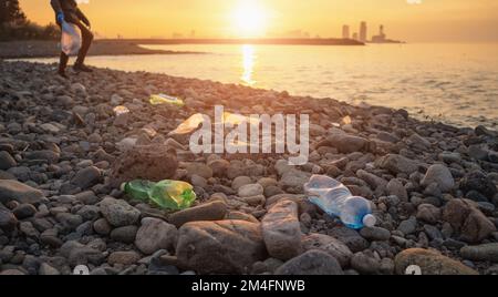 Verfahren zur Reinigung von Steinstränden aus Kunststoffabfällen. Ein Mann hebt Plastikflaschen in einem Müllsack auf. Umweltverschmutzungskonzept. Stockfoto