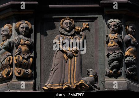 Vergoldete Renaissance-Dame mit Hund zu Füßen zwischen männlichen und weiblichen Grotesken auf dem aufwändigen orielen Fenster des Hauses zum Goldenen Ochsen in Vorstadt 17 in der Altstadt von Schaffhausen, Nordschweiz. Das ehemalige Gasthaus wurde von 1608 bis 9 in ein elegantes Stadthaus für die Familie Hageloch umgewandelt, mit seiner spätgotischen Fassade, die mit einem goldenen Ochsen und Figuren aus der babylonischen und griechischen Antike geschmückt ist. Stockfoto