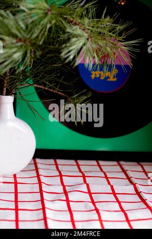 Fotoweiß und rote Tischdecke auf dem Tisch, darauf steht eine weiße Vase mit einem Zweig Tannen Stockfoto