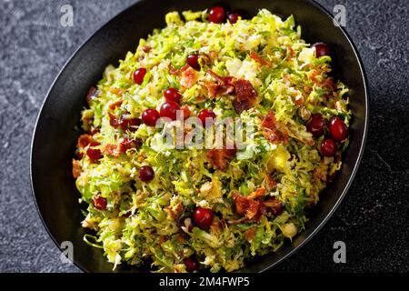 rosenkohl, Krautsalat mit Mandeln, knuspriger gebratener Speck und Cranberries in schwarzer Schüssel auf Betontisch, Nahaufnahme Stockfoto