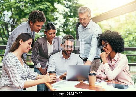 Es braucht ein Team, um das Geschäft zum Laufen zu bringen. Ein Team von Kollegen, die während einer Besprechung im Freien gemeinsam ein Notebook verwenden. Stockfoto
