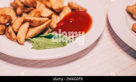 Gebackene Kartoffelspalten und Tomatensoße auf dem Tisch Stockfoto