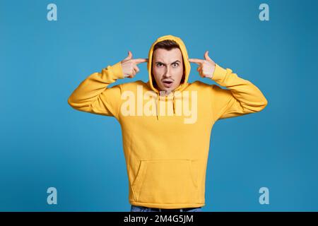 Schockierter Mann in gelbem Sweatshirt, der seine Finger an den Schläfen hält Stockfoto