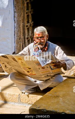 Ein alter Mann mit Brille liest Zeitung in den Straßen von Jaisalmer. Stockfoto