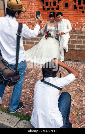 Professioneller Fotograf mit Begleiter, der mit dem Lichtmesser ein Hochzeitsfoto des vietnamesischen Paares vor der Kathedrale Notre Dame, Ho Chi Minh City, V, macht Stockfoto