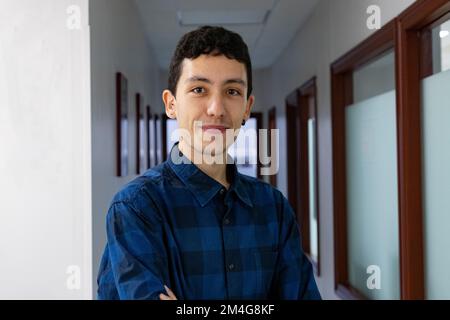 Porträt eines lächelnden jungen Weißen mit gekreuzten Händen in einem langen Flur, der ein blau-schwarz kariertes Hemd trägt. Porträtfotografie. Modell Stockfoto