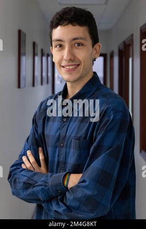 Porträt eines lächelnden jungen Weißen mit gekreuzten Händen in einem langen Flur, der ein blau-schwarz kariertes Hemd trägt. Porträtfotografie. Modell Stockfoto