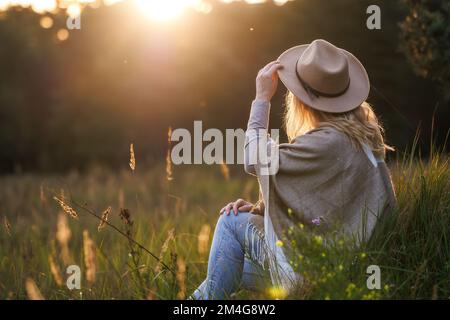 Glückliche Frau mit Hut und Poncho, die sich bei Sonnenuntergang im Freien entspannen kann. Psychisches Wohlbefinden und Ruhe in der Natur Stockfoto