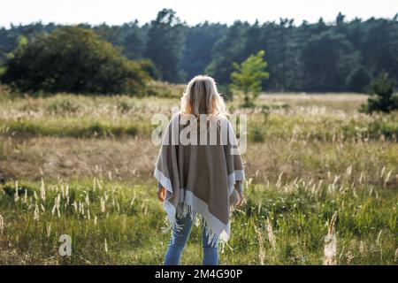 Boho Frau mit Poncho steht draußen. Genießen Sie es, Zeit in der Natur zu verbringen Stockfoto