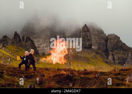 Isle of Skye, Schottland, Vereinigtes Königreich. 24.. Okt. 2021. Eine Person mit einer Boris-Johnson-Maske und eine andere mit einem Öltank als Kopf, die Ölfirmen repräsentiert, benutzt einen Flammenwerfer, um einen Baum zu verbrennen, der den letzten Baum auf Erden darstellt. Dieser theatralische Protest wurde von Ocean Rebellion, einer Schwesterbewegung des Aussterbens Rebellion, im Old man of Storr auf der schottischen Isle of Skye vor dem Start der COP 26 in Glasgow inszeniert. Stockfoto