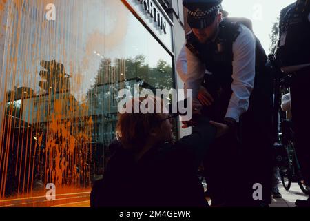 London, Großbritannien. 16 OKT, 2022. Aktivisten von Just Stop Oil bedeckten den Aston Martin Showroom in der Park Lane mit orangefarbener Farbe und blockierten die Straße. Mitglieder der Öffentlichkeit ziehen Aktivisten, die die Straße blockieren. Polizeibeamte verhaften einen Aktivisten, nachdem Farbe über ein Autoaufführungs-Fenster geworfen wurde. Stockfoto
