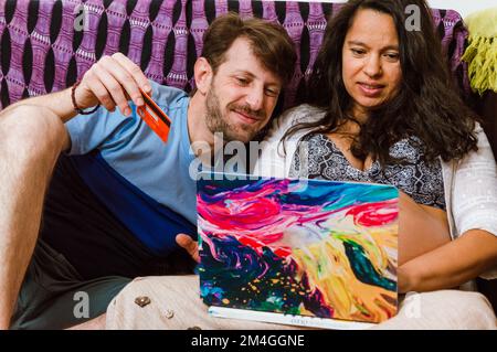 Vorderansicht eines erwachsenen lateinischen Paares von Mann und schwangeren Frau, das beim Online-Shopping auf dem Sofa auf dem Laptop sitzt. Stockfoto