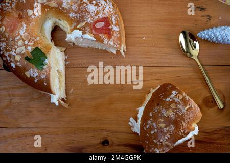 Roscon de reyes gefüllt mit Sahne, Brötchen oder Kuchen, typisch für Spanien, am 3. Königstag mit einer Portion auf schwarzem Teller und schwarzem Hintergrund. Stockfoto