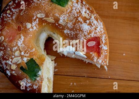 Roscon de reyes gefüllt mit Sahne, Brötchen oder Kuchen, typisch für Spanien, am 3. Königstag mit einer Portion auf schwarzem Teller und schwarzem Hintergrund. Stockfoto