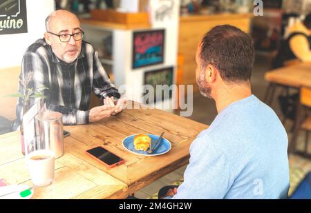 Zwei Erwachsene Männer mit Bart, die in einer modernen Cafeteria über ernste Dinge reden Stockfoto