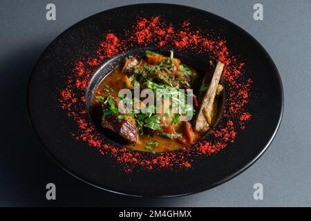 Eintopf mit Gemüse, Rinderrippchen und Koriander auf schwarzem Teller im Restaurant Stockfoto