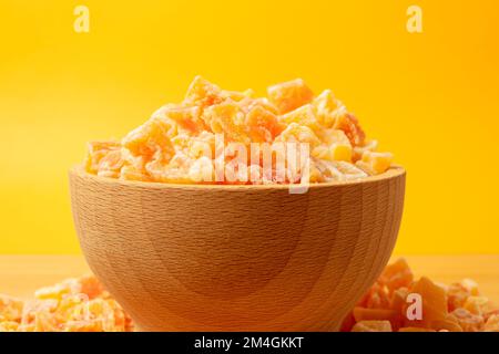 Gewürfelte kandierte Papaya in Schüssel auf Holzbrett. Gelber Hintergrund dahinter. Stockfoto