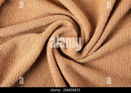 Gestrickter beigefarbener Hintergrund. Nahaufnahme einer Strickdecke. Wellenförmig faltet Material. Strickpullover oder -Mantel in warmem Beige. Stockfoto