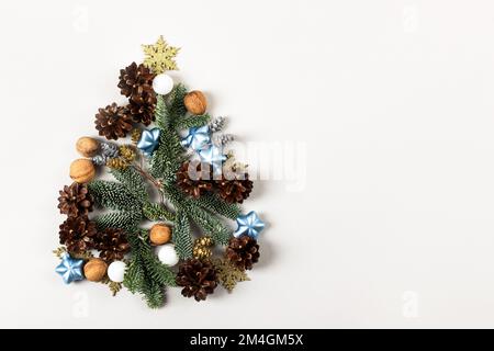 Kreative Weihnachtskomposition in Form eines Weihnachtsbaums auf grauem Hintergrund, bestehend aus Kiefernzapfen, Zweigen eines Weihnachtsbaums, Ziergegenständen Stockfoto