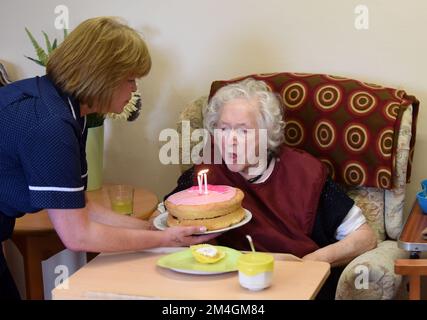 Pflegeheim-Assistentin feiert einen weiteren Geburtstag, während sie Kerzen auf Geburtstagskuchen ausbläst Großbritannien 2016 Stockfoto