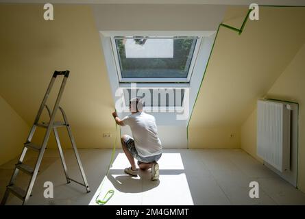 Painter entfernt Klebeband und erstellt einen scharfen Rand zwischen einem gelb-weiß lackierten Teil einer Wand. Stockfoto