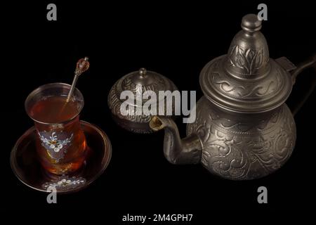 Teetasse mit Teekanne und Zuckerschale aus Metall, isoliert auf schwarzem Hintergrund Stockfoto