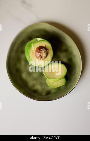 Top-Shot mit frisch geschnittener Avocado auf grünem Teller Stockfoto