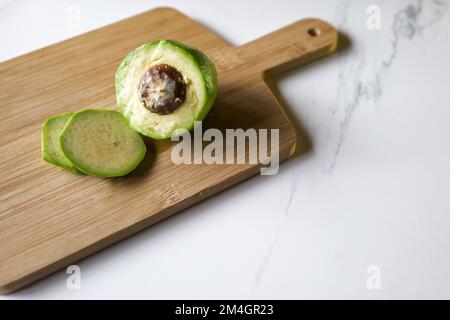Avocado geschält und geschnitten auf Holzbrett auf Marmorküche mit Toast im Hintergrund Stockfoto