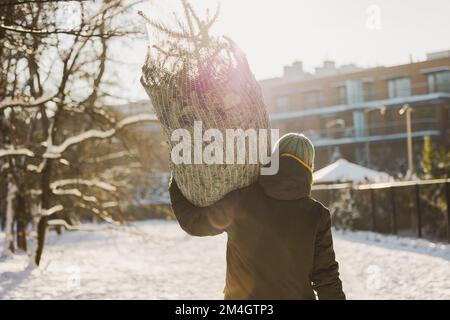 Ein Mann trägt einen Weihnachtsbaum auf den Schultern draußen Stockfoto