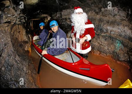 21. Dezember 2022, Sachsen-Anhalt, Wettelrode: Besucher aus Seesen lassen sich vom Weihnachtsmann auf eine Führung durch das Bergwerk Röhrigschacht im Seegen Gottes adit mitnehmen. Mit dieser Aktion überraschte das Team der Besuchermine seine Gäste. Seit etwa 20 Jahren bietet das Erlebniszentrum Bergbau Röhrigschacht Wettelrode längere Untergrundausflüge in einer Tiefe von ca. 300 Metern an. Seit einigen Jahren gibt es eine Tour, bei der ein Teil der Strecke von Paddelbooten befahren wird. Die ersten Bergleute begannen vor etwa 800 Jahren, in der Region Mansfeld nach Kupfererz zu graben. Seit dem Jahr 1750 war carrie Bergbau Stockfoto