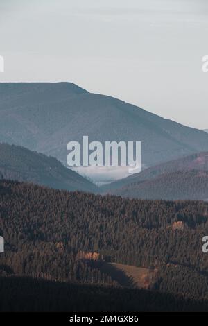 Blick auf einen weißen Nebel in einem Tal zwischen zwei Bergen im Herzen des Beskydy-Gebirges, Tschechische Republik. Das Morgenlicht beleuchtet die Bucht Stockfoto