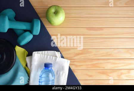 Gesunder Lebensstil mit Heimsportgeräten wie Kurzhanteln, Gewichten, Gummibändern und gesundem Essen auf einer Matte auf einem Holzlattboden. Stockfoto