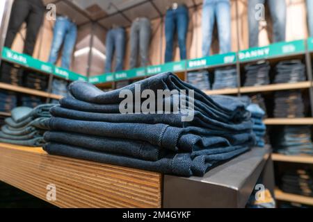 Nahaufnahme von vielen Jeans in den Regalen im Laden. Ein Haufen Jeans auf dem Regal. Konzept des Einkaufs, Verkaufs, Einkaufs und Jeans. Stockfoto