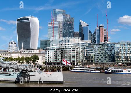 HMS Belfast Museumsschiff mit City of London Skyline von Büroblöcken im Hintergrund. Das markante geschwungene Gebäude mit weißen Seiten im Hintergrund ist Stockfoto