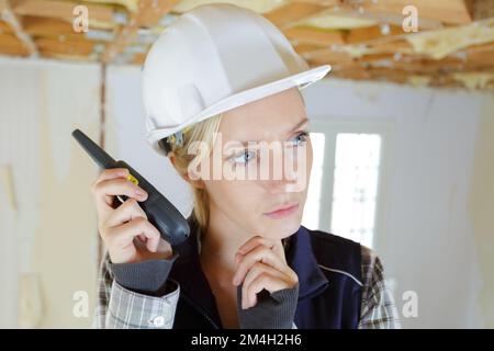 Junge Frau mit Helm, die auf dem Walkie-Talkie spricht Stockfoto